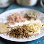 A plate of Bhutanese food: dark buckwheat noodles, pale noodles, red rice and a round buckwheat pancake