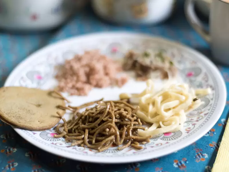A plate of Bhutanese food: dark buckwheat noodles, pale noodles, red rice and a round buckwheat pancake