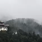 Jakar Dzong on its ridge in Bumthang, with cloud drifting through the forest