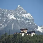 Gasa Dzong above the forest, under a snow-covered peak