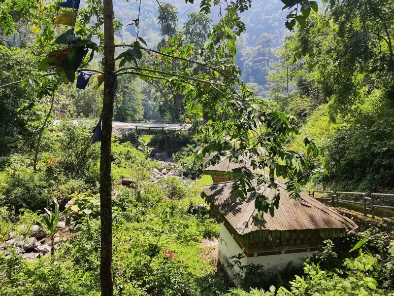 Forest and a traditional roofed building beside the river at Nganglam, in the south of Pemagatshel