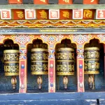 A row of brass prayer wheels in painted niches at Changangkha Lhakhang in Thimphu