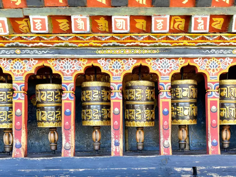 A row of brass prayer wheels in painted niches at Changangkha Lhakhang in Thimphu