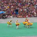 Masked dancers in yellow skirts on the festival ground at Thimphu Tshechu, in front of the crowd