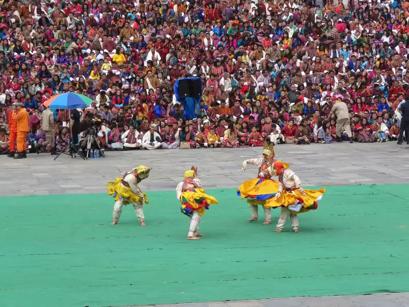 Masked dancers in yellow skirts on the festival ground at Thimphu Tshechu, in front of the crowd