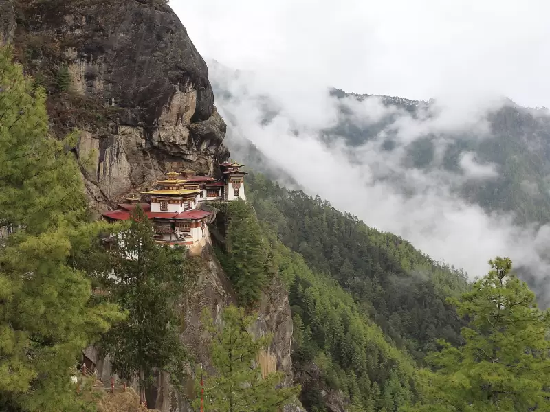 Taktsang, the Tiger's Nest, on its cliff with cloud drifting through the forest below