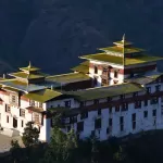 Trashigang Dzong lit by the sun against a dark hillside