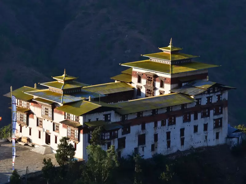 Trashigang Dzong lit by the sun against a dark hillside